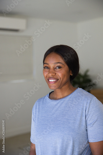 Obraz na plátne African woman standing and smiling at home, wearing blue tee beside air conditio