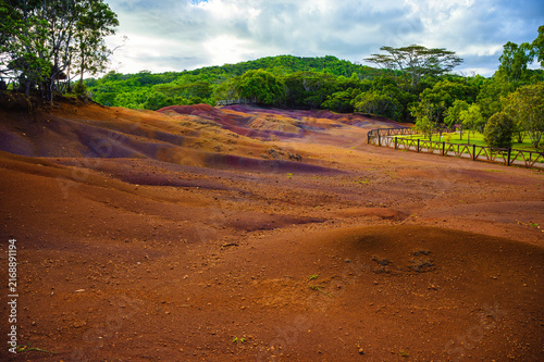 Cuadro en lienzo Vibrant red, brown, and purple sand dunes at Seven Colored Earth in Chamarel Geopark, Mauritius, bordered by tropical rainforest under dramatic clouds