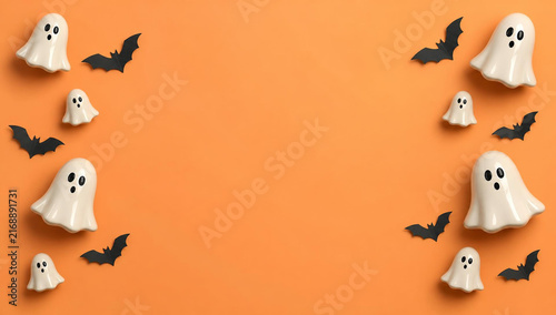 Halloween background with cute ceramic ghosts and black paper bats arranged on an orange surface, flat lay composition with copy space for text