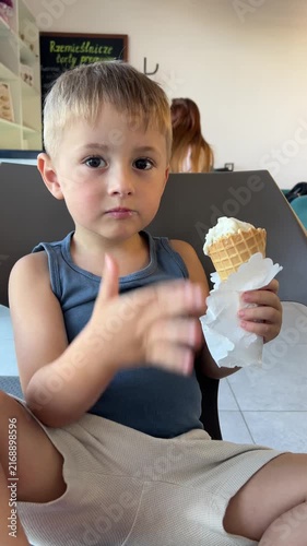 Little boy eating delicious ice cream in waffle cone at cafe