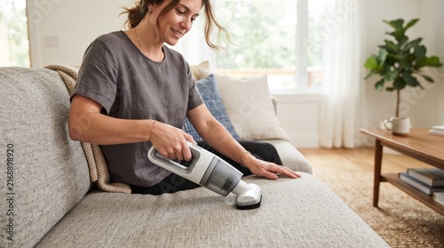 Woman Cleaning Sofa: A woman uses a handheld vacuum cleaner to clean her sofa, demonstrating a modern approach to home maintenance and comfort.