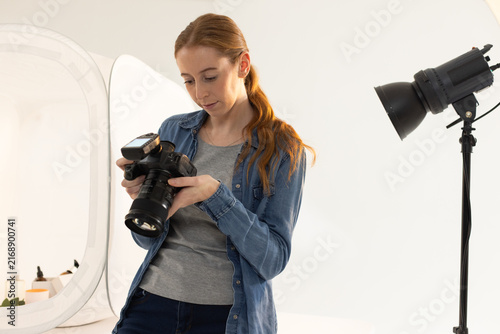 Woman in twenties wearing denim shirt holding DSLR camera and adjusting strobe beside reflector