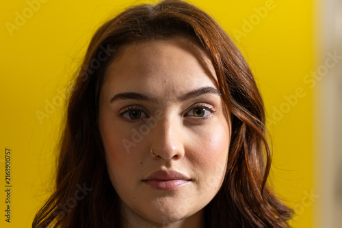 Adult female posing in studio against yellow backdrop, showing small hoop nose ring and wavy hair