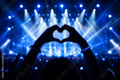 Concert crowd hands forming heart gesture under stage lights
