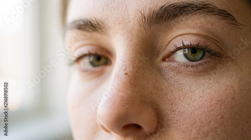 A close-up shot focuses on the expressive eyes and textured skin of a young woman, revealing a sense of introspection and quiet contemplation.