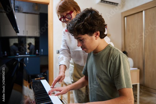 Teen boy taking piano class with patient woman teacher in a home music lesson