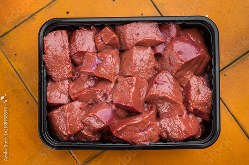 Bild auf Leinwand Raw diced beef veal liver in tray on yellow tile surface with copy space