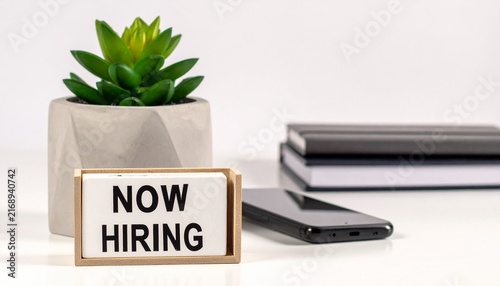 Small Flip Calendar Displaying NOW HIRING Text on White Desk with Potted Succulent Plant and Office Supplies