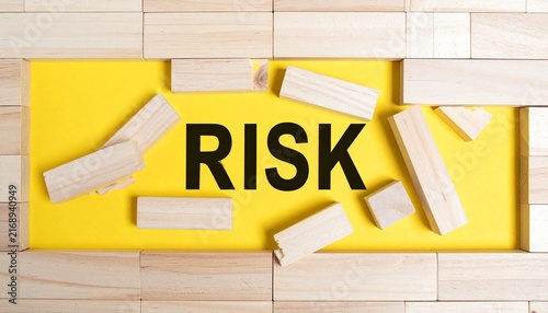 The Word RISK Framed by Scattered Wooden Blocks and Fallen Wooden Bricks on Bright Yellow Background
