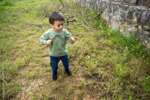 Little boy having fun playing with a dry branch in the countryside in Hidalgo, Mexico.
