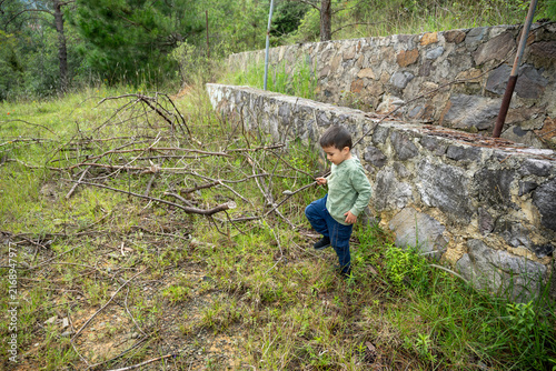 Niño pequeño jugando con ramas secas en el patio de una casa de campo en Hidalgo, México.