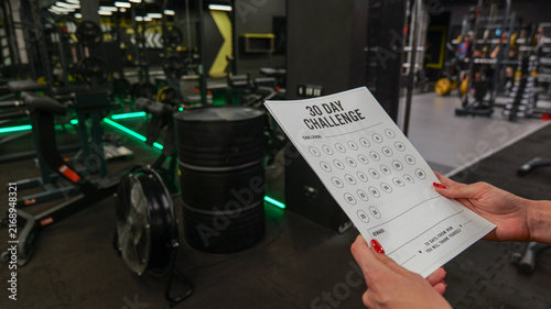 Foto Woman holding a 30-day fitness challenge tracker in a modern gym setting