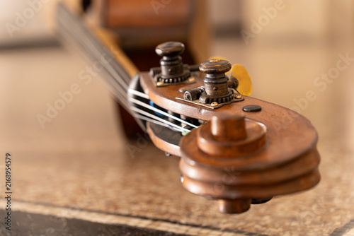 Detailed close-up of a vintage double bass scroll and tuning pegs. Elegant wooden texture of an old contrabass musical instrument with selective focus and warm background.