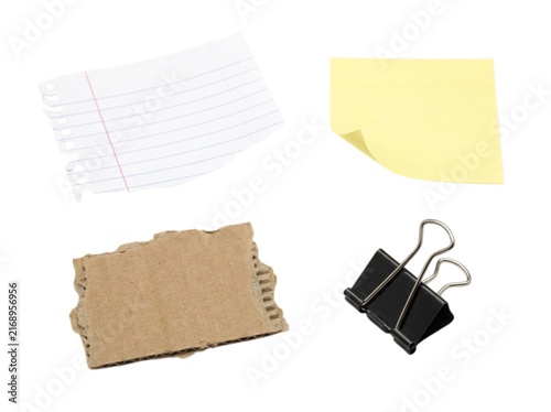 A collection of office supplies including a lined notebook paper, a yellow sticky note, a piece of torn cardboard, and a black binder clip isolated on white background