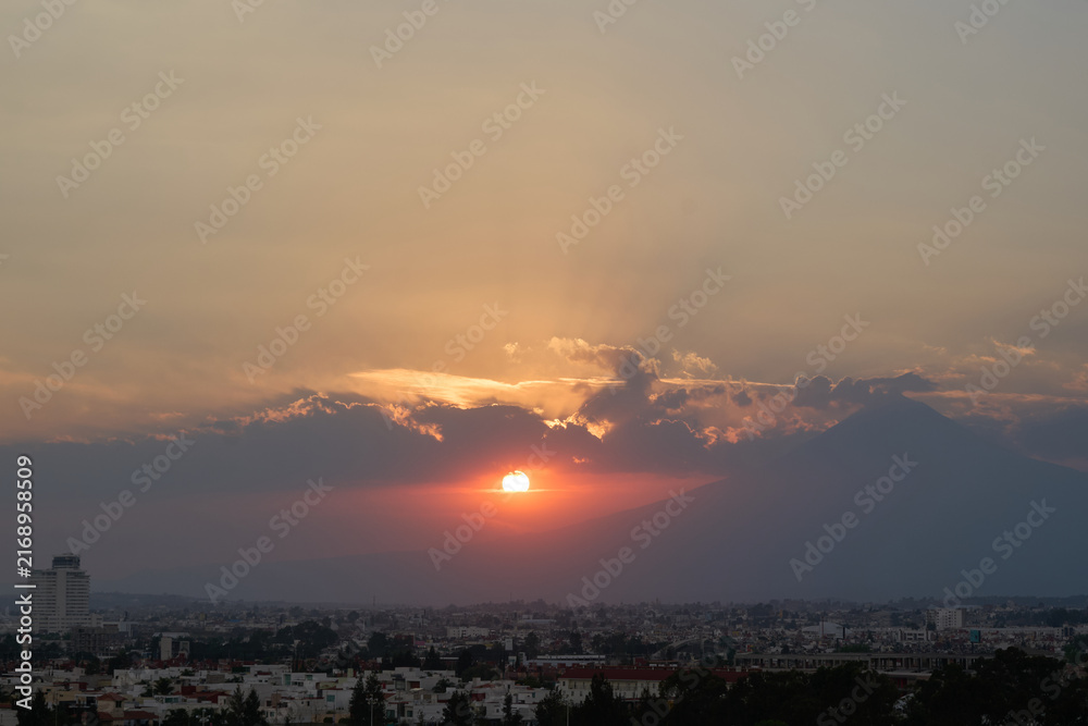 Fototapeta premium Golden sunset in Puebla with Popocatépetl’s silhouette amid clouds and warm light
