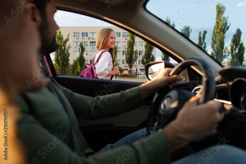 Foto Girl with backpack heading to school as parents watching from car, creating warm