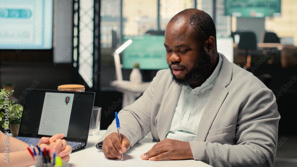 Fototapeta premium African American candidate signs a new employment contract and shares a handshake after accepting a new position within a successful business corporation with agreement on legal terms and onboarding.