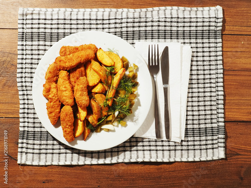 Foto Golden brown fried chicken tenders sit beside crispy potato wedges on a white plate