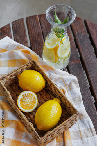 Fotografie Top view of fresh lemons in a basket beside a glass carafe with lemon slices and