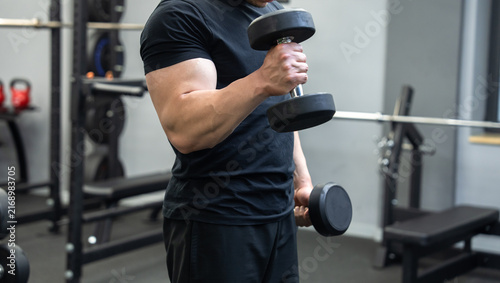 Cuadro en lienzo A muscular man is standing in the gym, holding dumbbells, training