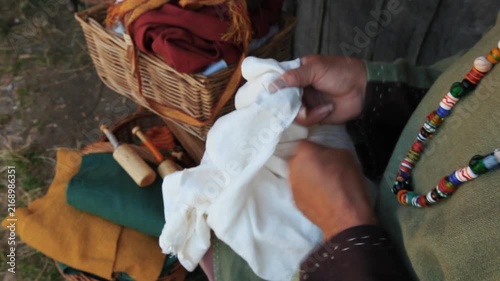 Hands of medieval reenactor in period costume hand sewing linen fabric, close-up historical craft