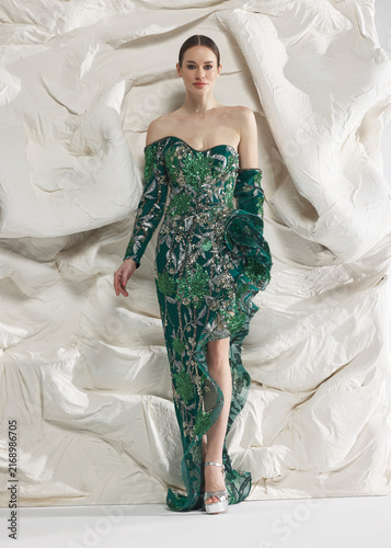 Woman in emerald green sequin evening gown with high slit in studio