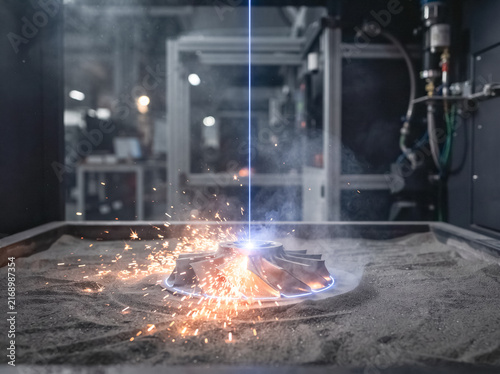 3D Printing Process: A high-tech 3D printer uses a laser to precisely fuse powder particles, creating an intricate metal component in a controlled industrial environment.