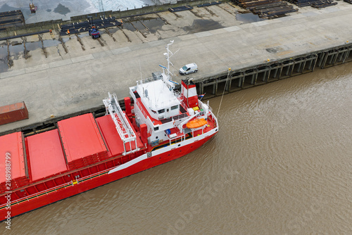 Bild auf Leinwand Red Cargo Ship at Industrial Dockside Loading Steel in Morning Light