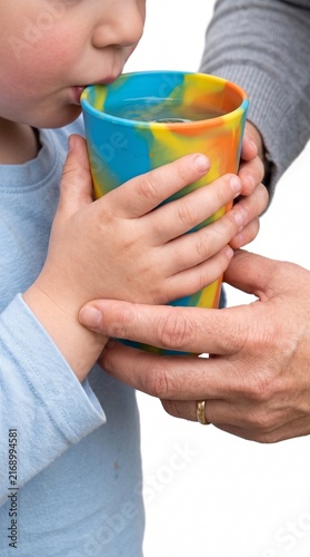 A child drinking water from a colorful cup held by an adult