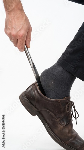 Using a shoehorn to put on a brown leather dress shoe with a grey sock