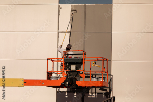 Man on manlift painting a commercial building with a long pole and paint roller