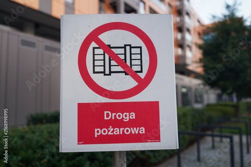 Close-up view of Polish fire route safety sign stating Droga pozarowa with prohibition symbol in front of modern apartment building blurred background.