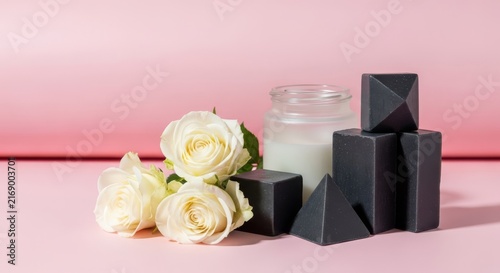 Pristine white roses beside geometric charcoal soaps and a frosted glass jar on a pale pink backdrop. Elegant minimalist luxury wellness still life, elegant, organic, bathroom