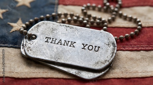 Military dog tags featuring a thank you message resting on a weathered American flag to honor the courage and sacrifice of veterans and active duty service members