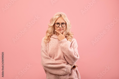 Konstfotografi Thoughtful Young Caucasian Woman With Glasses Pondering With Hand On Chin, Standing In Studio With Pink Background