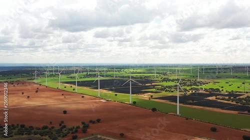 Majestic wind turbines rise harmoniously against lush fields and dark earth, showcasing nature's blend with technology in this peaceful landscape under a cloudy sky.