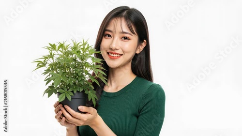 Young Woman Holding Potted Plant: A smiling young Asian woman, with long dark hair and wearing a green top, holds a small potted green plant, symbolizing growth and natural beauty.