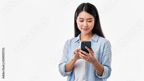 Young Woman Using Smartphone: A focused young woman with long dark hair, dressed in a casual light blue shirt, intently uses her smartphone, her fingers navigating the screen with precision.