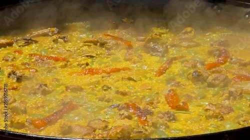 Close up of traditional Spanish paella boiling in large pan during cooking contest in slow motion.