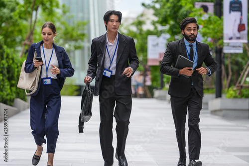 Canvas Print Three young business professionals wearing conference badges walk together carry