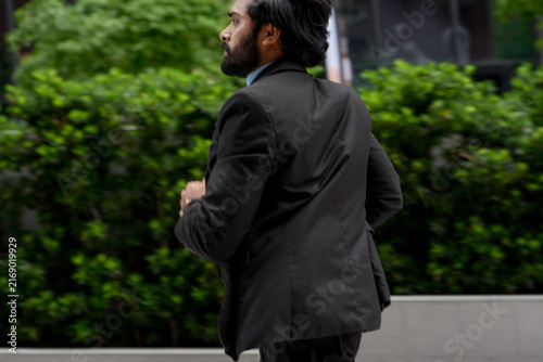 фотографія A young Indian businessman checks the time mid stride while running to work unde