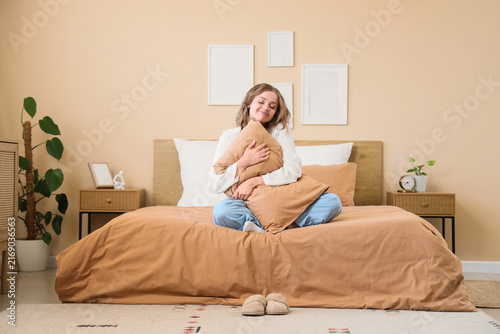 Comfort and relaxation at home, young woman embracing a pillow while sitting ...