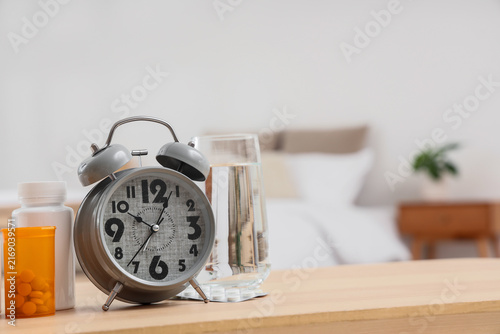 Obraz na plátne Alarm clock with pill bottles and glass of water on table in bedroom
