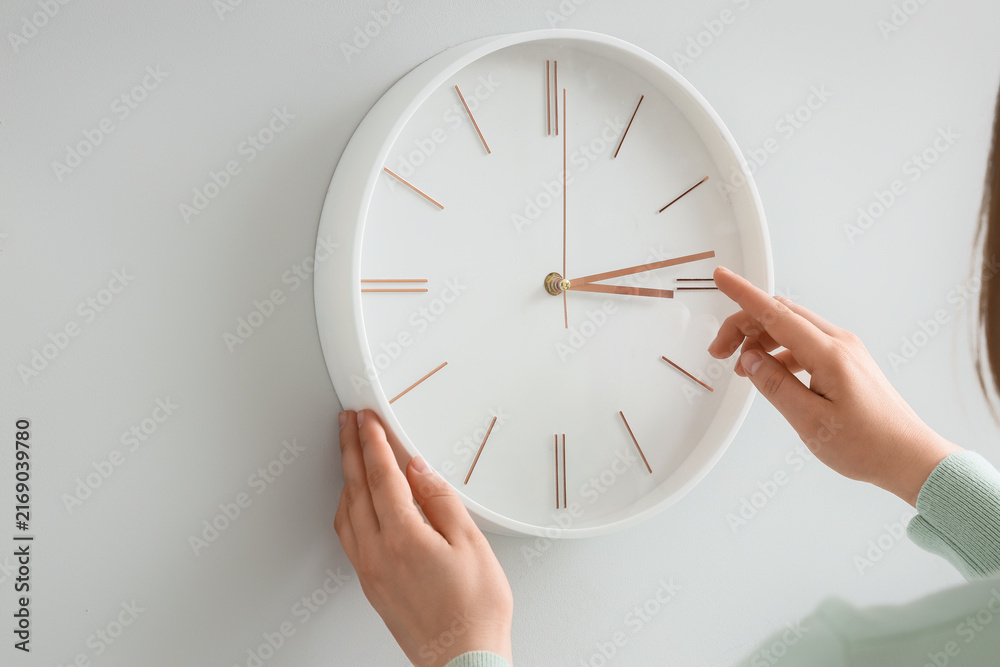 Naklejka premium Woman setting time on wall clock at home, closeup. Daylight saving time concept