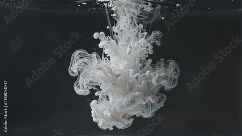 White ink swirls gracefully underwater against a deep black backdrop.