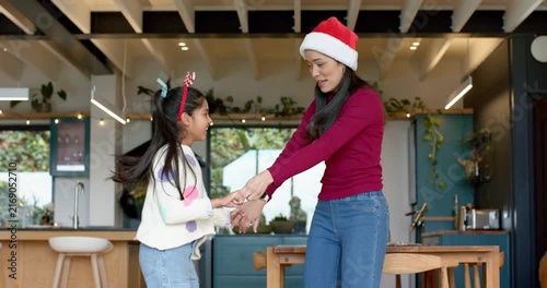 Facing each other mother and daughter dancing in Santa hat and candy cane headband in kitchen