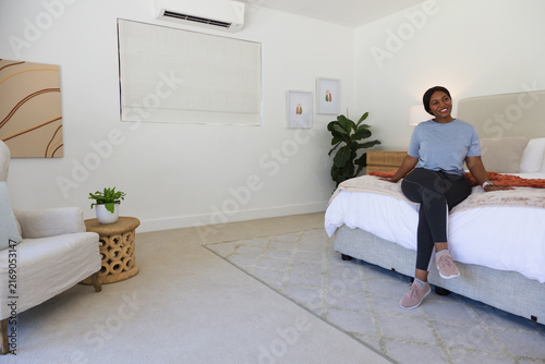 African American woman sitting on right of bed with white duvet and coral throw, copy space