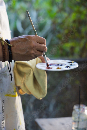 Obraz na płótnie Senior Asian man holding round palette and mixing paint with brush wearing apron