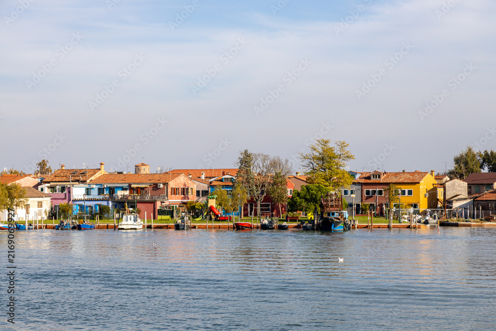 Obraz premium View of Burano's colorful waterfront houses and moored boats, seen from Mazzorbo, Venice, Italy