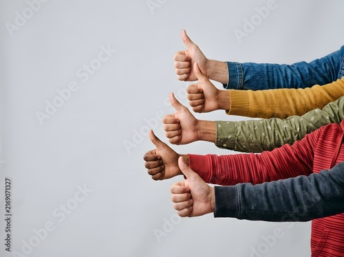 Four Diverse Hands Raised in Unity Giving Bright Thumbs-Up Against Minimalist Light Gray Background